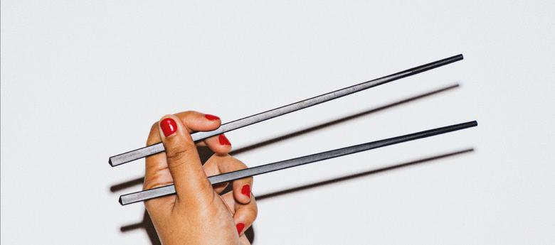 Hand holding chopsticks against a light wall